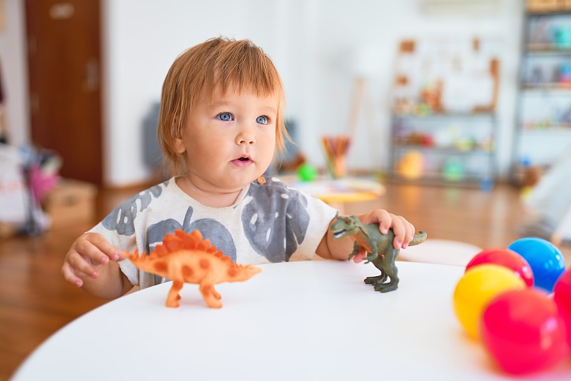 可爱的幼童玩恐龙周围的玩具在幼儿园