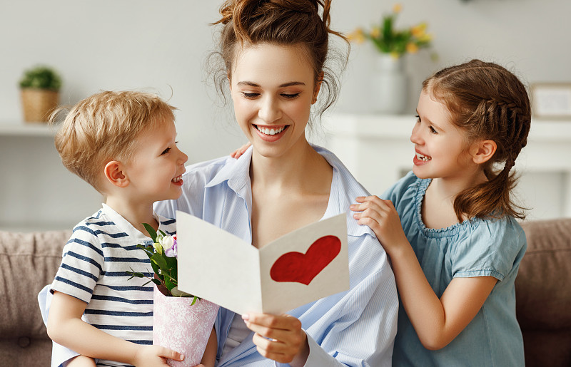 在明亮的公寓里，兴奋的孩子们和年轻女子拿着鲜花读着手工制作的节日卡片