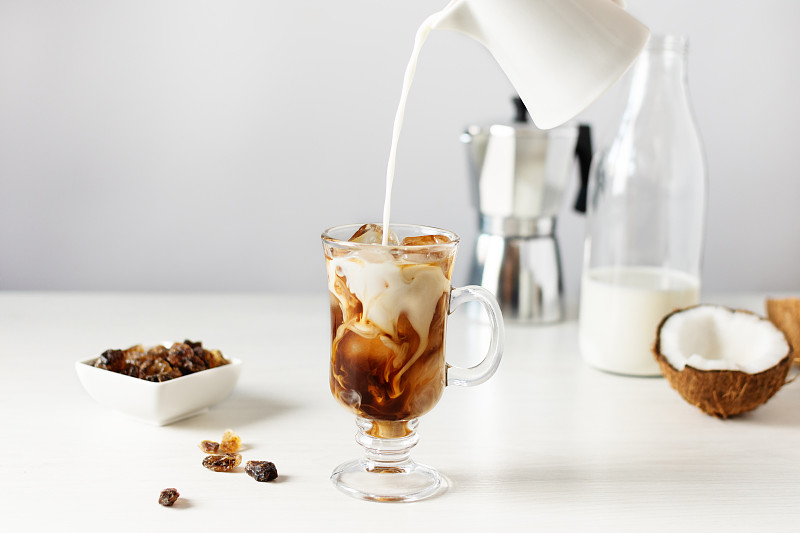 将椰奶倒入杯中加入冰咖啡。