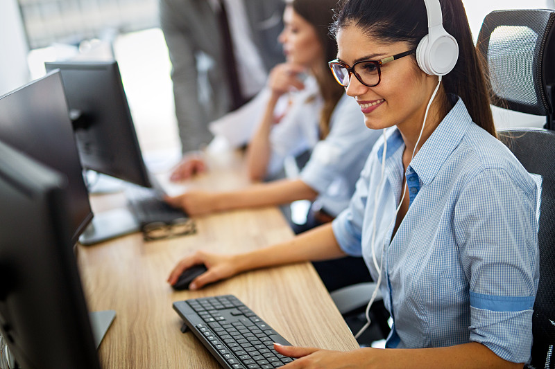 在呼叫中心，一位戴着耳机的友好的年轻女性热线接线员