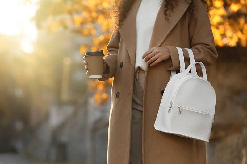 年轻女子与时尚的白色背包和热饮户外晴天，特写