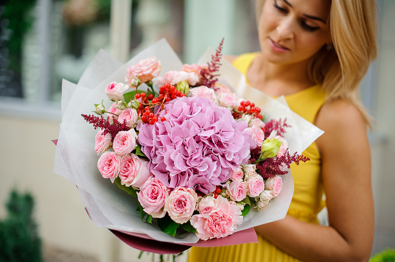 女性拿着一束玫瑰，astilba，康乃馨的包装纸