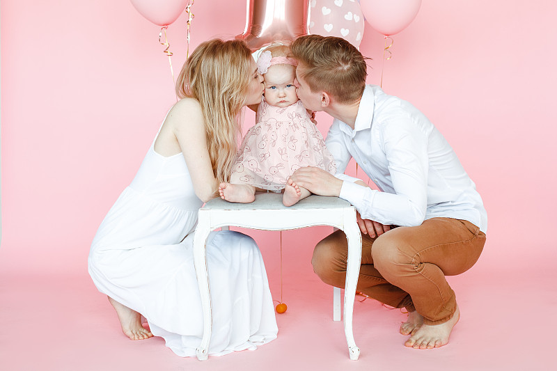 平静，充满爱的男人，女人亲吻一岁的婴儿坐在椅子上庆祝生日聚会