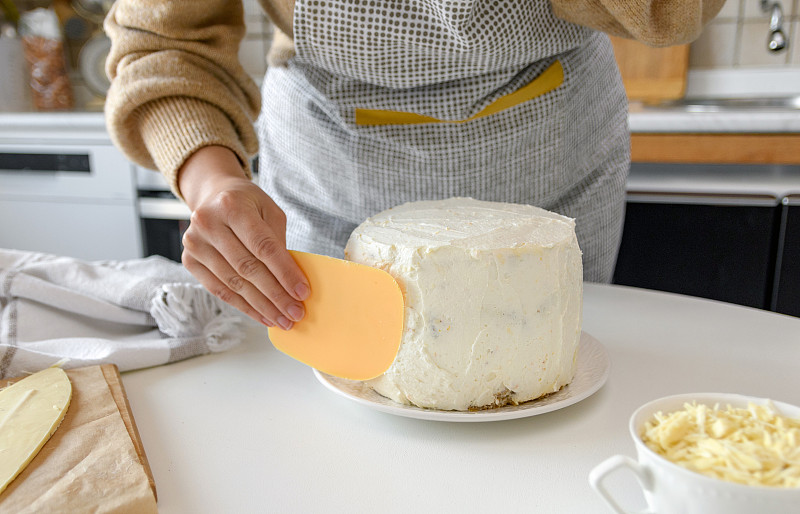妇女在家里的厨房里用抹刀在蛋糕上涂糖霜。