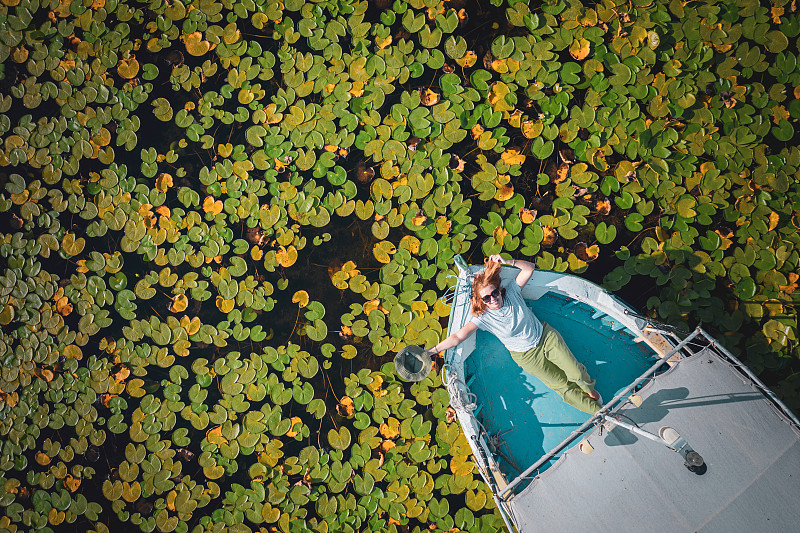 鸟瞰一名快乐的女游客躺在船在莲花睡莲湖中间。