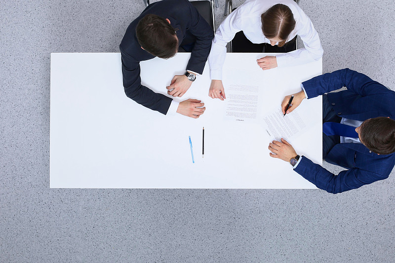 一群商人和律师坐在桌子旁讨论合同文件，从上面看。商人正在签署协议后的文件