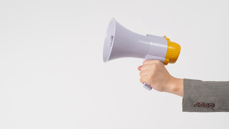 手握扩音器，白色背景穿灰色西装。