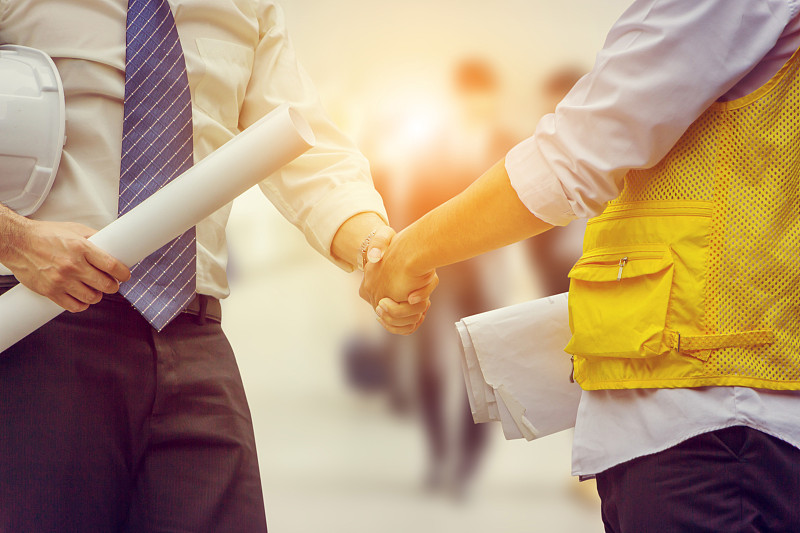 成功和幸福的概念，商业工程师的人手里拿着图纸和握手在城市外的办公室。