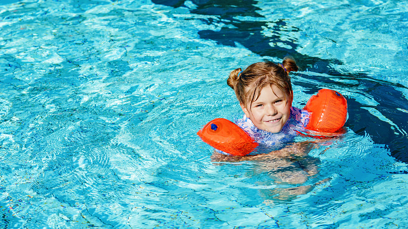 小学龄前女孩与保护游泳在户外游泳池玩日落。儿童在户外泳池学习游泳，嬉水，嬉笑，玩耍。家庭度假。