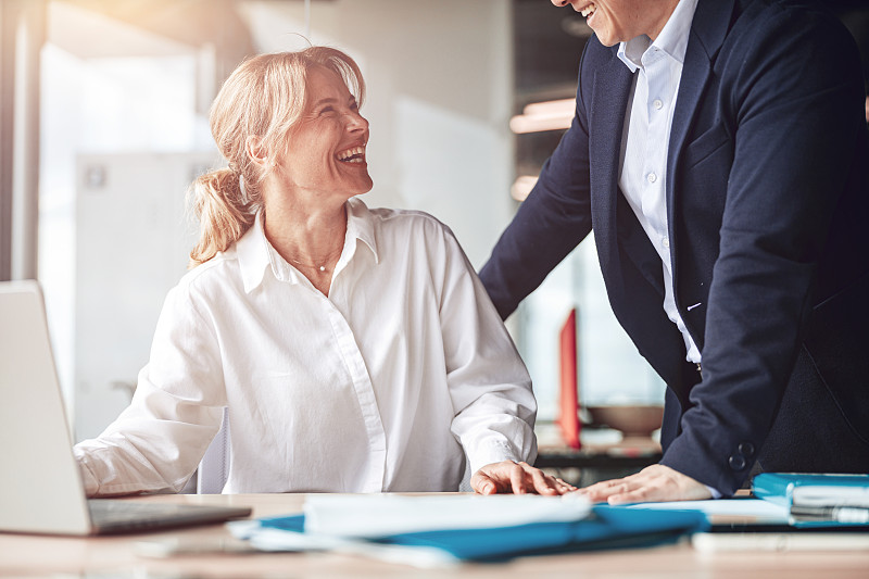 在现代明亮的办公室里，成熟的女商人微笑着用笔记本电脑与她的队友交谈