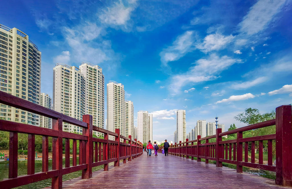 春日的清晨蓝天白云下小学生和市民通过红色的木栈道