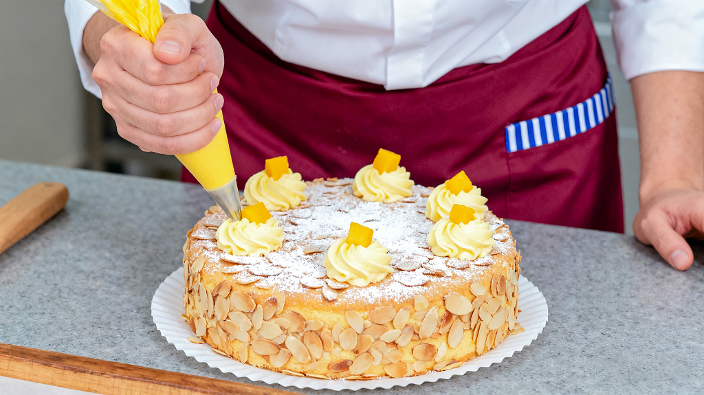 穿白衬衫和酒红色围裙的人正在装饰一个圆形蛋糕表面铺满杏仁片