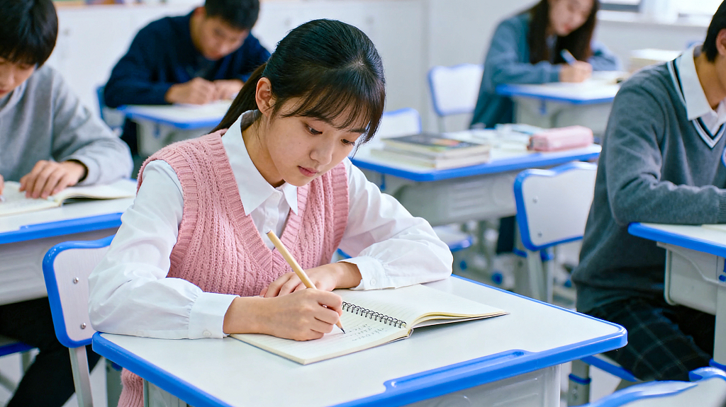 教室里学生们专注学习穿粉色针织背心女生低头认真在笔记本上书写
