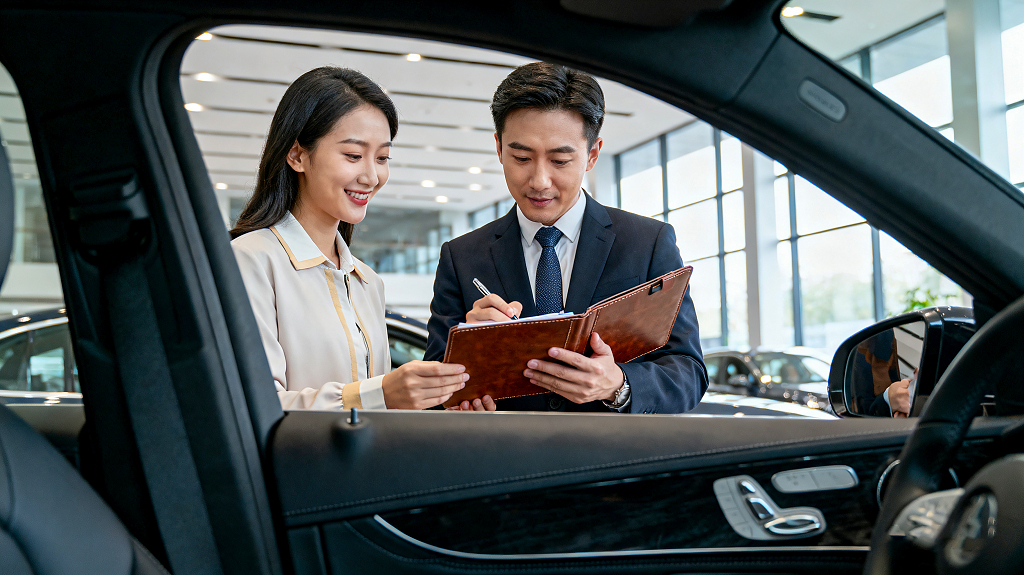 购车服务商务签订合同汽车4S店内展厅销售人员持文件夹与顾客洽谈