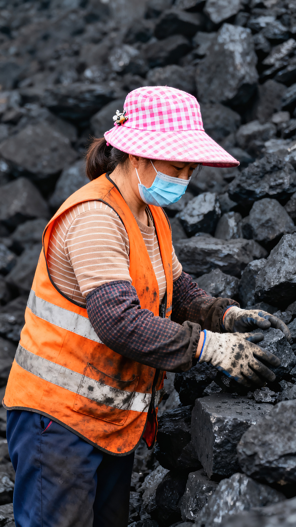 煤炭分拣工在煤堆旁从事体力劳作着反光背心戴口罩手套专注分拣