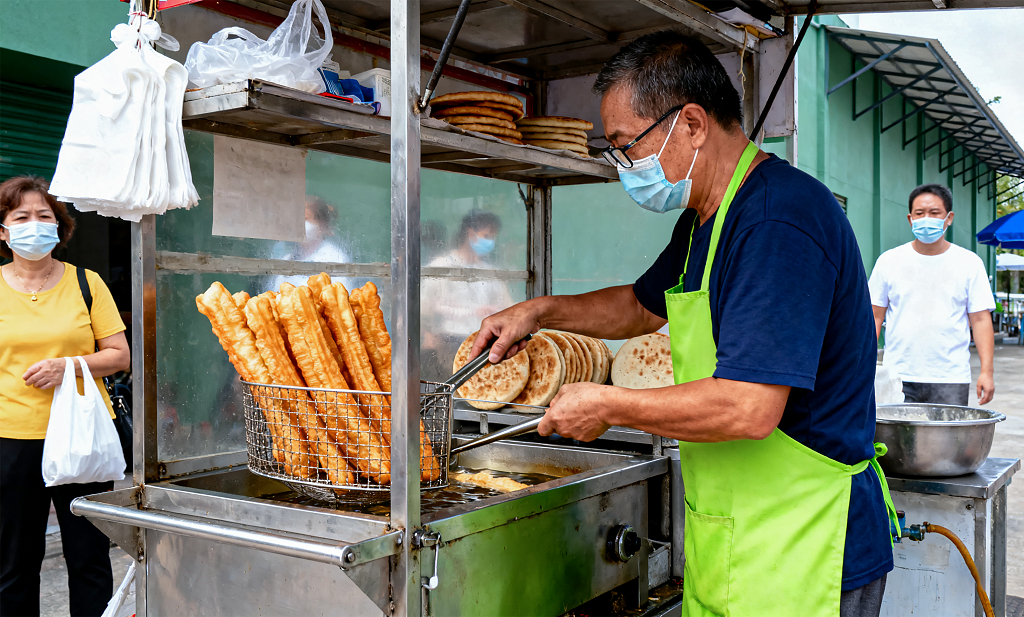 街头摊贩专注炸制油条顾客一旁等候市井餐饮场景忙碌且具烟火气