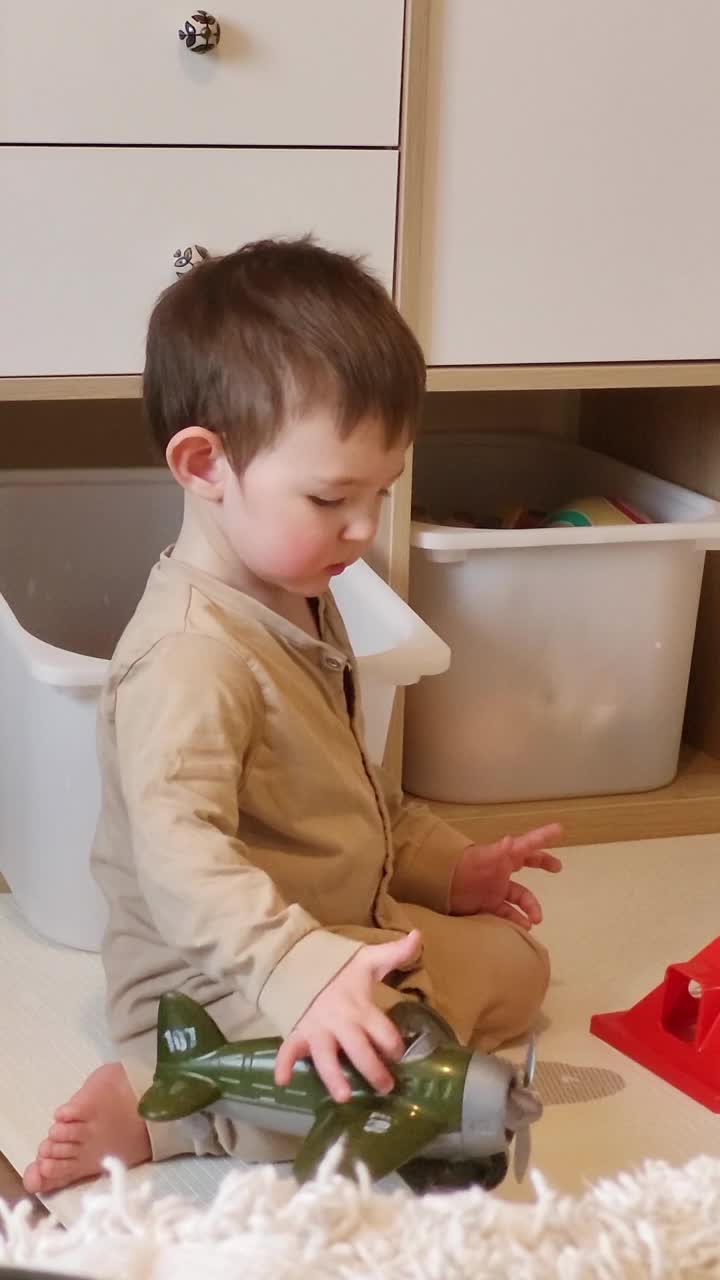 一个快乐的孩子坐在育儿室的地板上玩玩具。宝宝在家里玩游戏时微笑。1岁8个月(20个月)