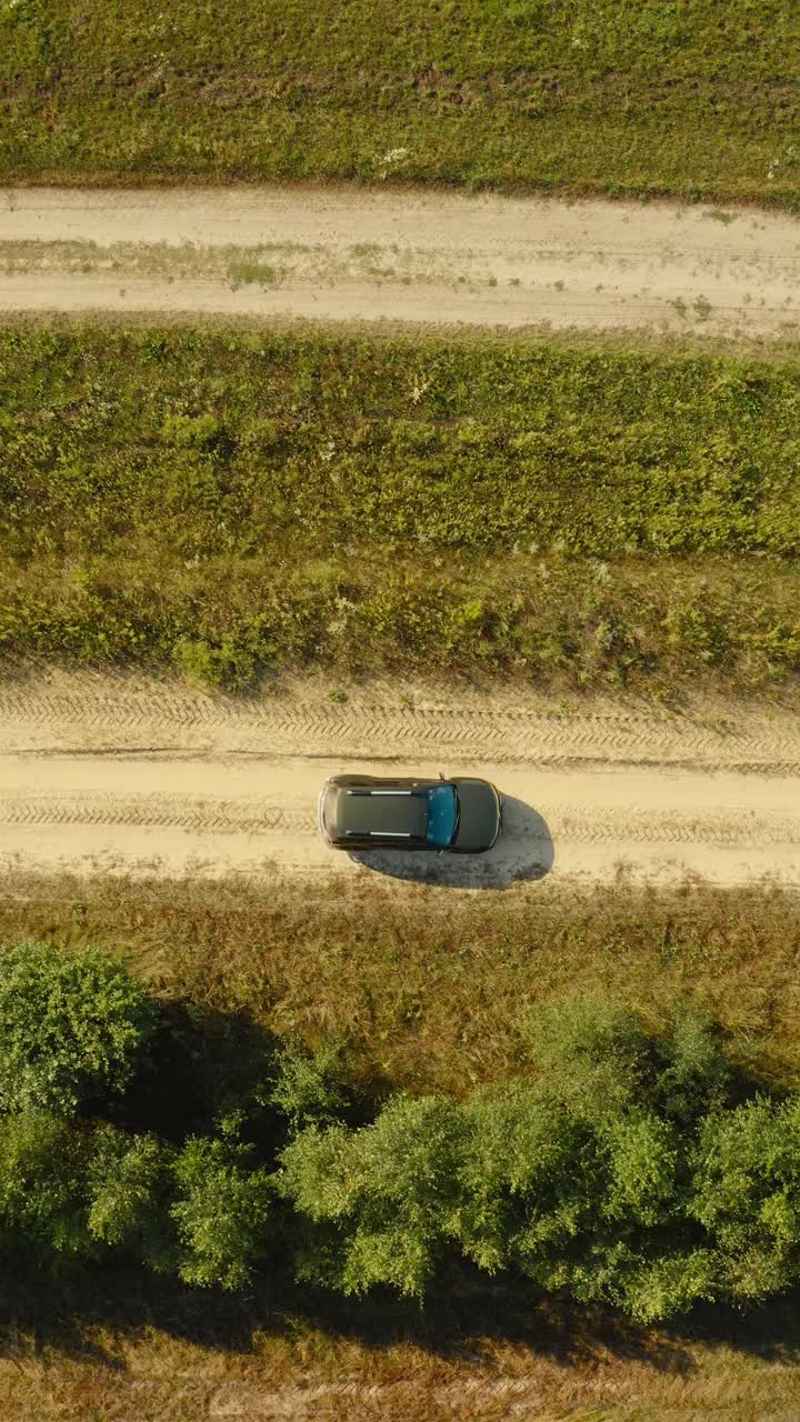 高架顶平视图的SUV汽车汽车SUV驾驶运动在农村道路通过夏季绿色田野。乡村景观。动态汽车驾驶
