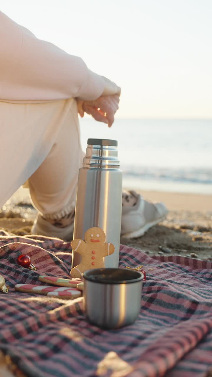 垂直视频。海边沙滩上的圣诞气氛。日出，毯子上有热茶和节日姜饼饼干。