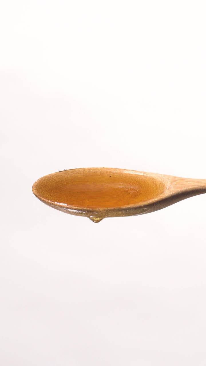 (实时和垂直)蜂蜜从木勺上掉下来