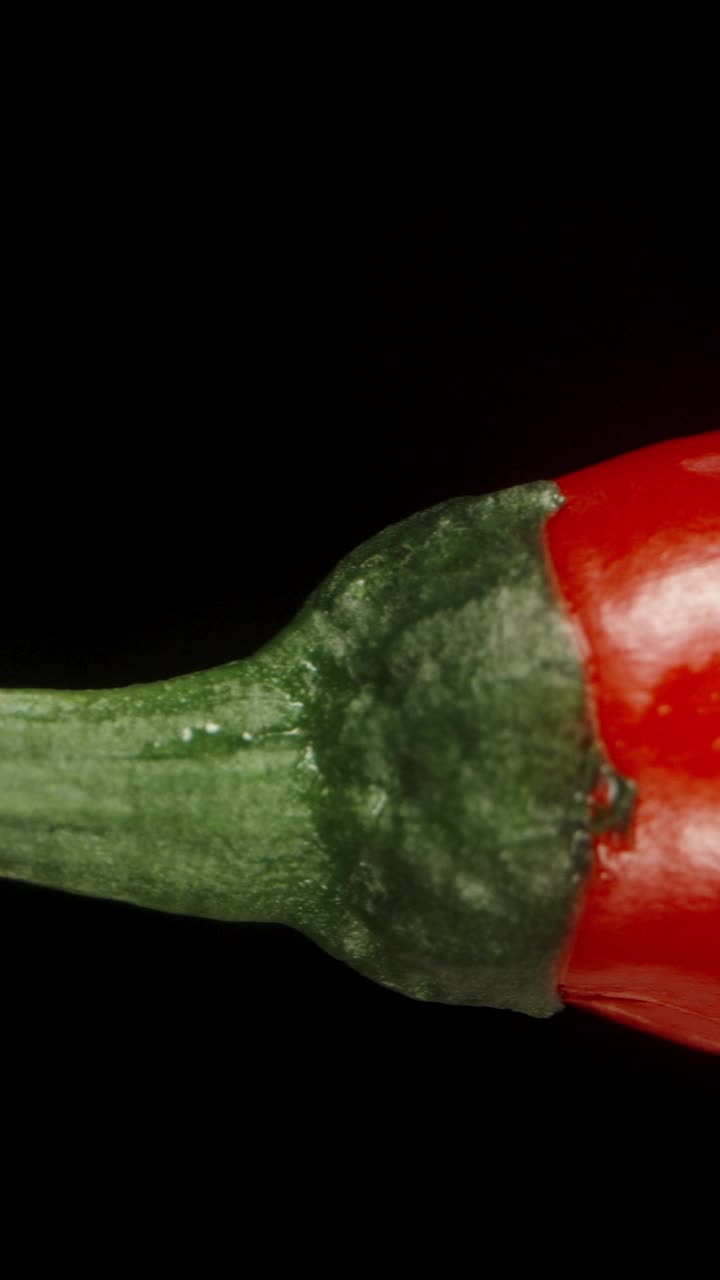 燃烧和辛辣的红辣椒辣椒，与水滴，隔离在黑色背景，微距幻灯片。垂直视频社交媒体