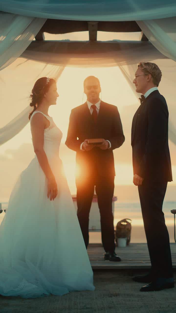 垂直画面:美丽的新娘和新郎在海边的户外婚礼上。多民族多元文化的浪漫情侣和好友的婚礼场所。