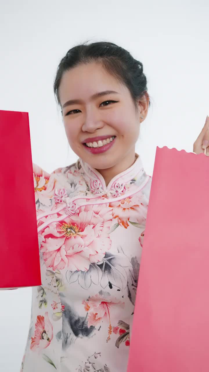 中国/亚洲妇女在中国新年期间，双手拿着红色和粉红色的购物袋，白色背景，穿着旗袍白色花卉图案连衣裙
