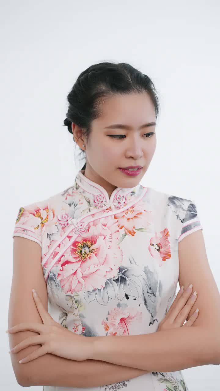 中国/亚洲妇女站在微笑，交叉手臂，看着镜头在中国春节期间，白色背景，穿着旗袍白色花卉图案的服装